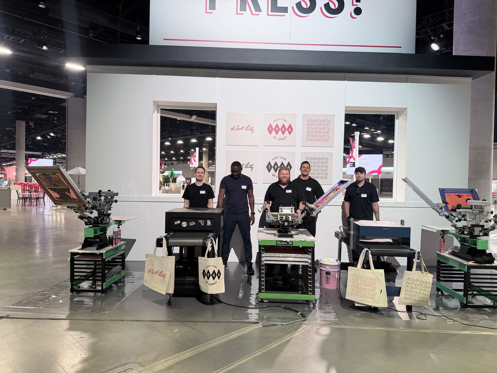 Merch Troop crew standing ready behind a row of presses at a large venue